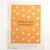 Orange tea towel with white AA logo, flying pigs and 'Kindness starts in the kitchen.'